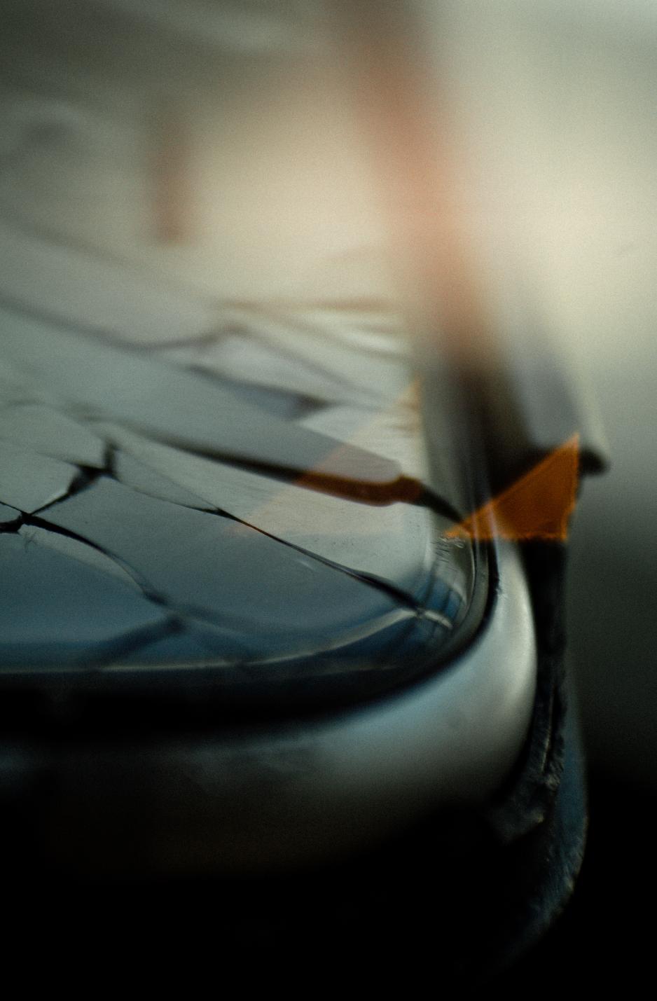 Abstract close-up of a cracked phone screen near a window, with soft blur and light streaks running vertically through the frame.