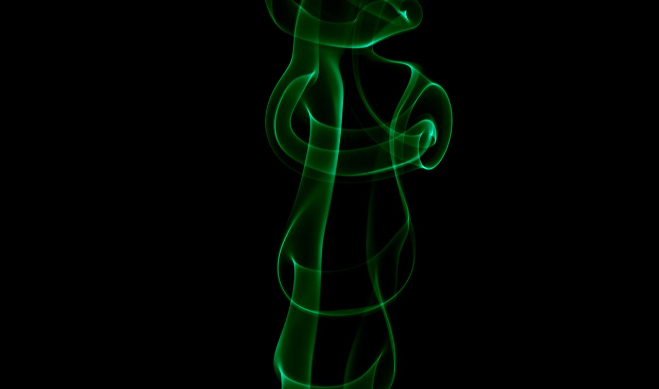 A single ribbon of incense smoke lit emerald green, caught mid curl against pure black.