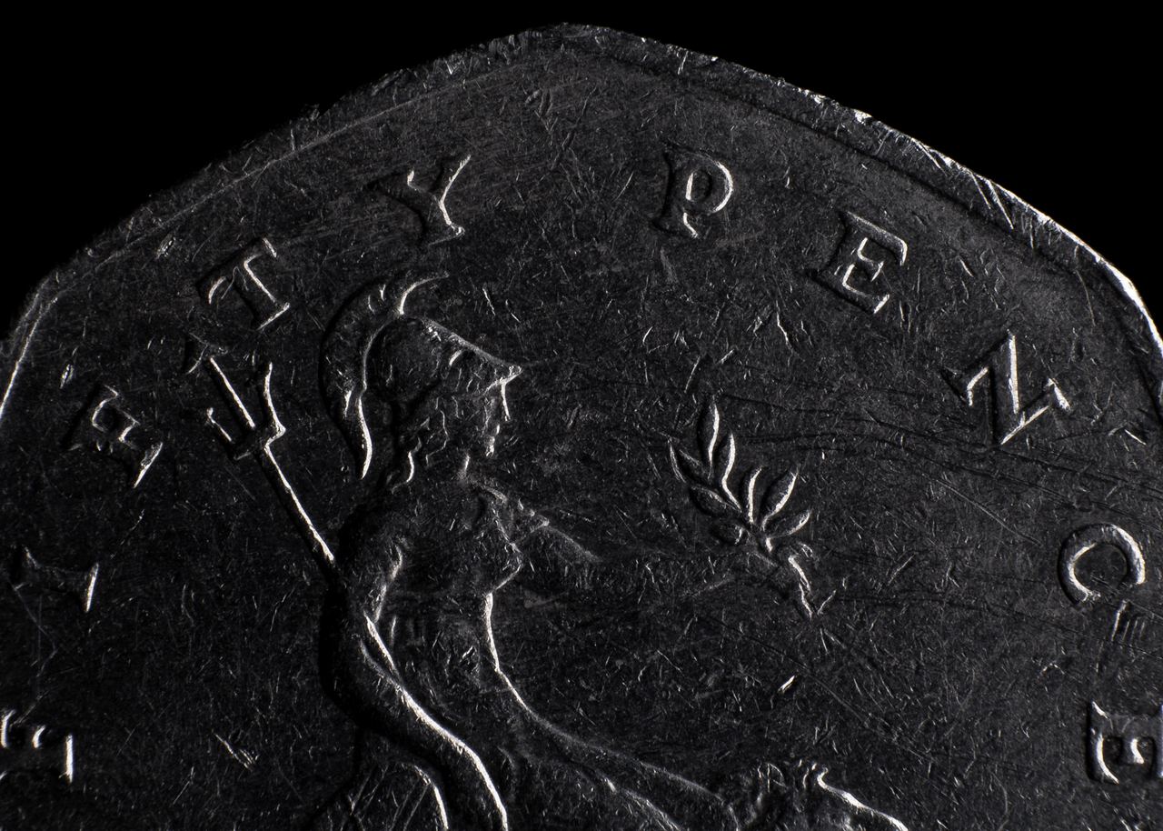 An extreme close up of an old fifty pence coin showing part of the seated Britannia figure, a lion, and the raised letters around the rim.